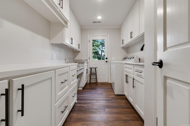 clothes washing area with cabinets, dark hardwood / wood-style flooring, ornamental molding, and washing machine and clothes dryer