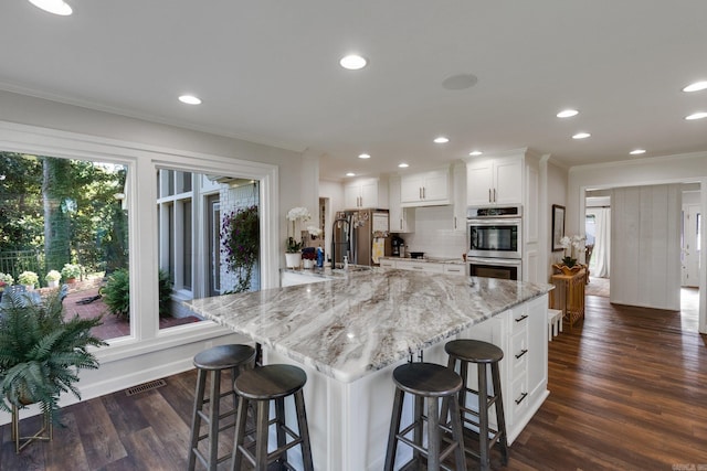 kitchen featuring a kitchen breakfast bar, white cabinetry, light stone countertops, and double oven