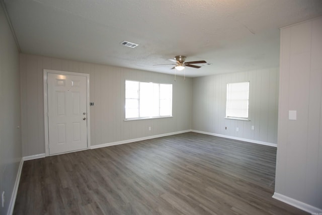 empty room with a textured ceiling, dark hardwood / wood-style floors, ceiling fan, and wooden walls