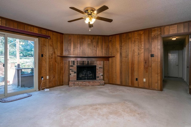 unfurnished living room featuring wood walls, a brick fireplace, ceiling fan, a textured ceiling, and light colored carpet