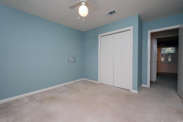 unfurnished bedroom featuring ceiling fan, light colored carpet, a textured ceiling, and a closet