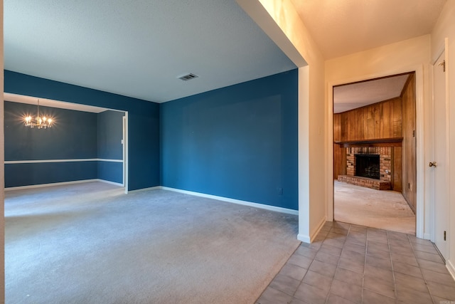 spare room featuring wooden walls, a fireplace, light carpet, and an inviting chandelier