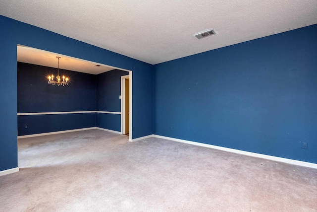 carpeted spare room with a textured ceiling and an inviting chandelier