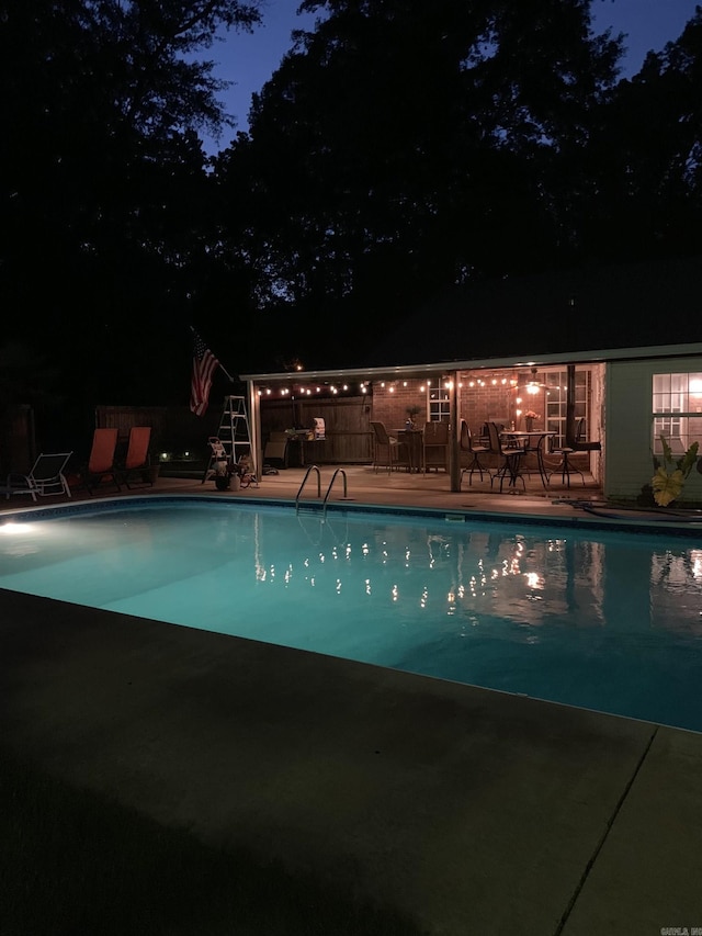 pool at night featuring a patio