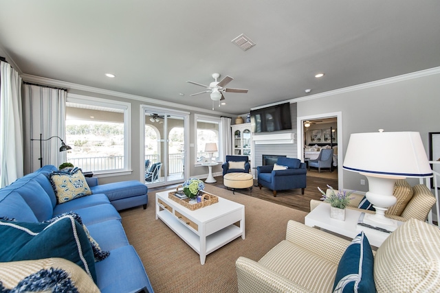 living room featuring ceiling fan, wood-type flooring, ornamental molding, and a fireplace