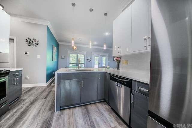 kitchen with sink, kitchen peninsula, decorative light fixtures, white cabinets, and appliances with stainless steel finishes