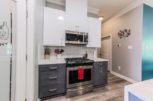 kitchen with dark wood-type flooring, white cabinets, crown molding, decorative backsplash, and stainless steel appliances