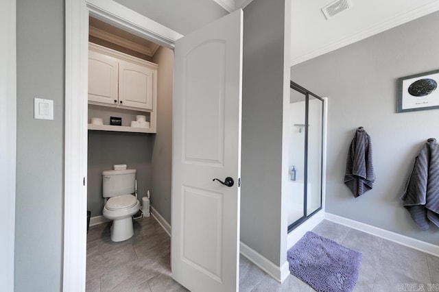 bathroom featuring toilet, a shower with shower door, and ornamental molding