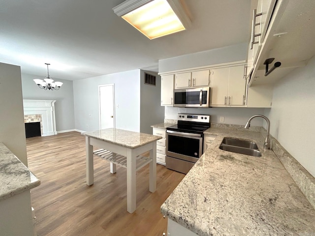 kitchen featuring pendant lighting, a tile fireplace, an inviting chandelier, sink, and appliances with stainless steel finishes