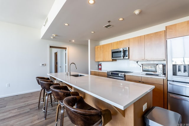 kitchen featuring sink, an island with sink, stainless steel appliances, and light hardwood / wood-style floors