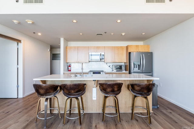 kitchen featuring light brown cabinetry, stainless steel appliances, hardwood / wood-style flooring, and an island with sink