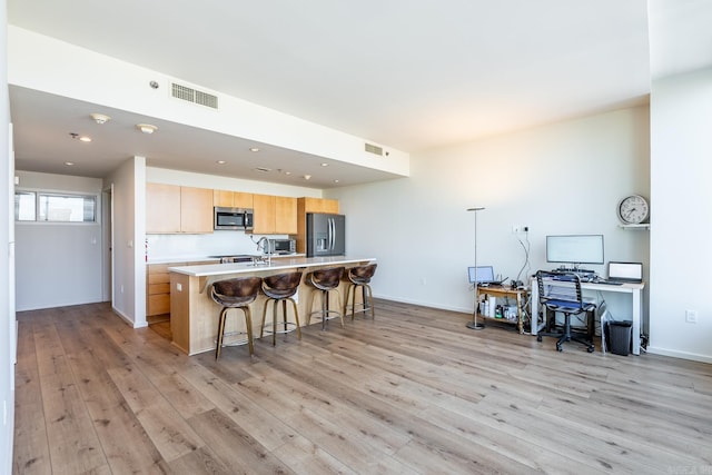 kitchen with light brown cabinets, light hardwood / wood-style flooring, an island with sink, a breakfast bar, and appliances with stainless steel finishes