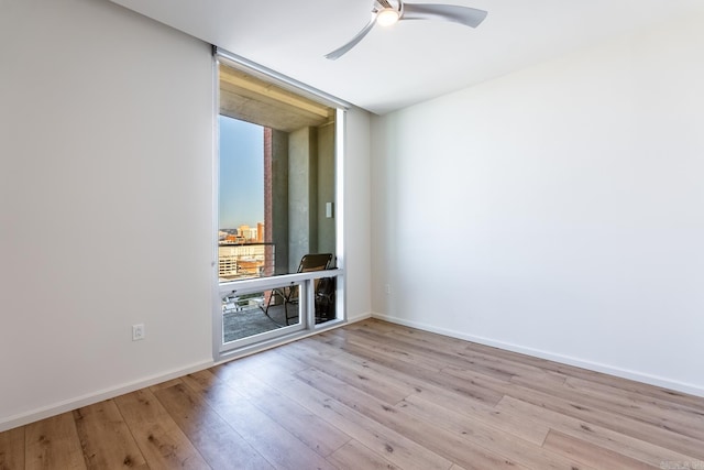 empty room with ceiling fan, expansive windows, and light wood-type flooring