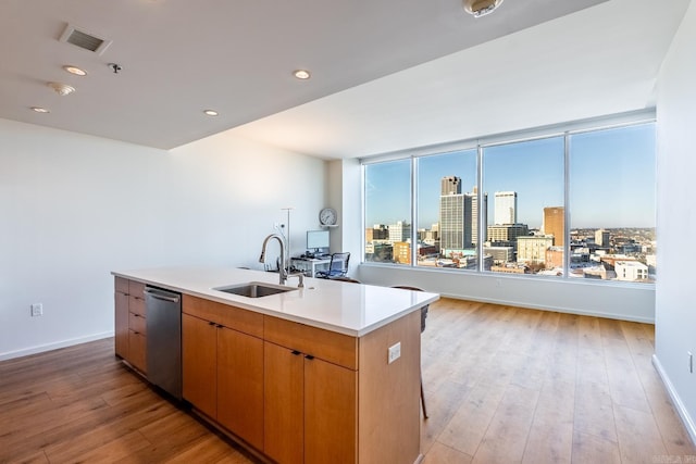 kitchen with stainless steel dishwasher, light hardwood / wood-style floors, sink, and an island with sink