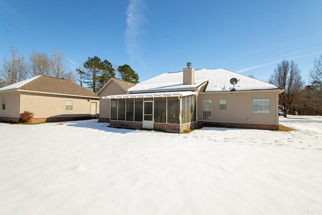 snow covered back of property featuring a sunroom