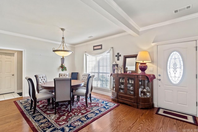 dining space with hardwood / wood-style floors, beamed ceiling, and ornamental molding