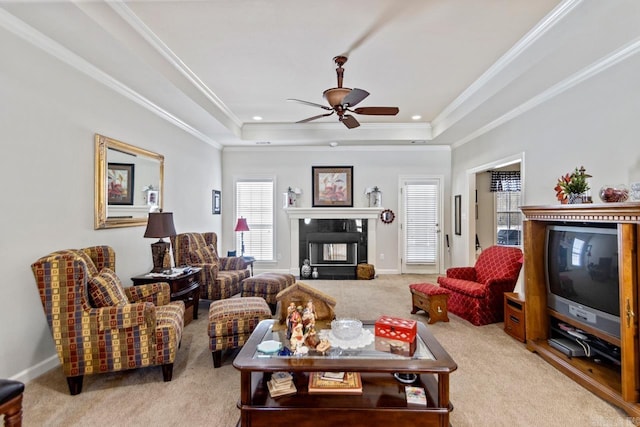 carpeted living room with a raised ceiling, ceiling fan, and ornamental molding