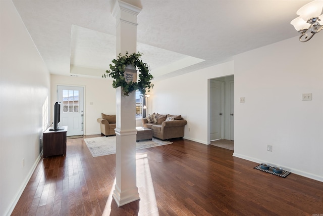 unfurnished living room with a raised ceiling, ornate columns, and dark wood-type flooring