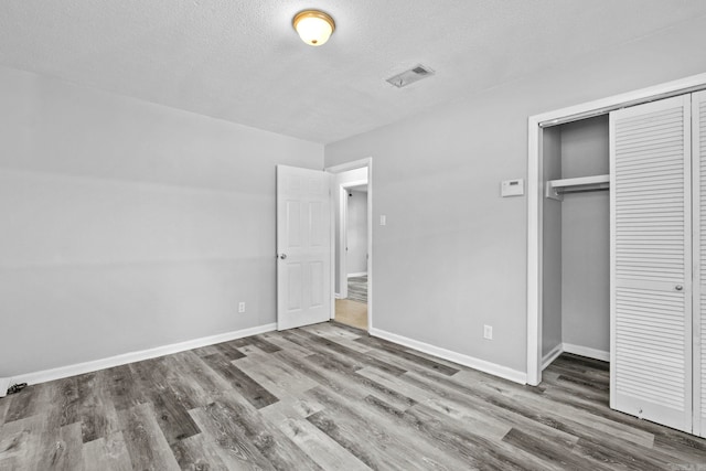 unfurnished bedroom featuring a closet, wood-type flooring, and a textured ceiling