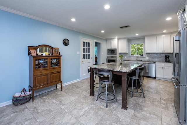 kitchen featuring decorative backsplash, light stone countertops, stainless steel appliances, white cabinets, and a kitchen island