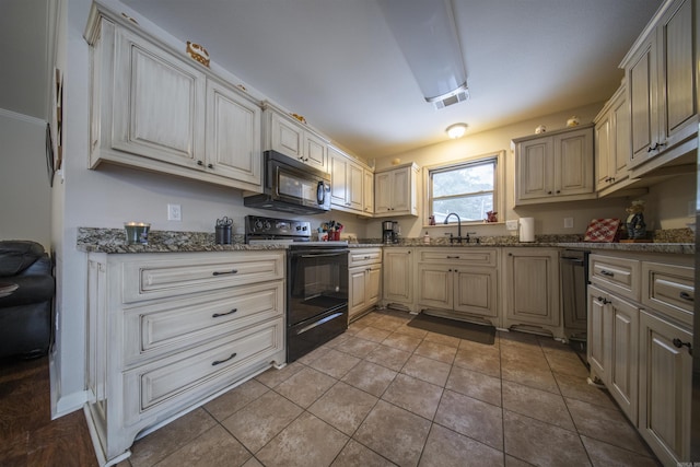 kitchen with dark stone countertops, sink, light tile patterned floors, and black appliances