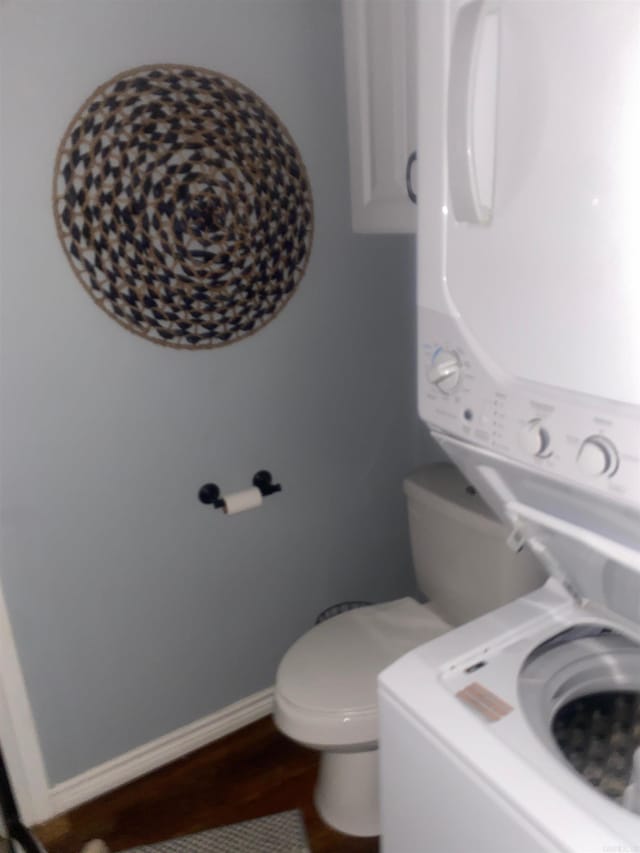 bathroom with stacked washer / dryer, hardwood / wood-style flooring, and toilet