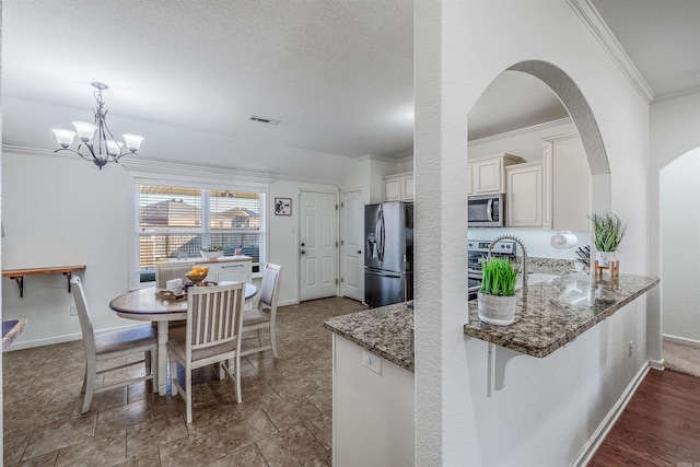 kitchen featuring appliances with stainless steel finishes, kitchen peninsula, dark stone counters, pendant lighting, and a notable chandelier