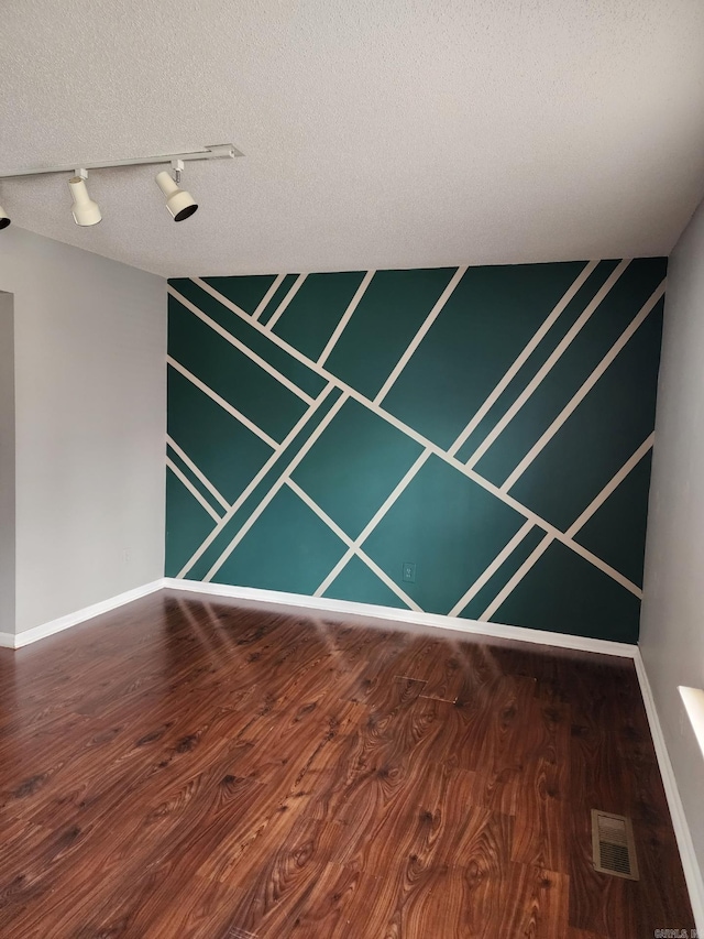 unfurnished room with dark wood-type flooring, a textured ceiling, and rail lighting