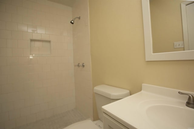 bathroom with a tile shower, vanity, and toilet