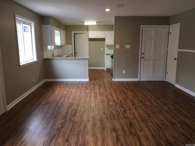 interior space featuring kitchen peninsula, light stone countertops, dark wood-type flooring, white cabinets, and sink