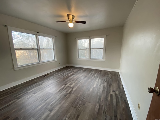 unfurnished room featuring dark wood-style floors, baseboards, visible vents, and a ceiling fan