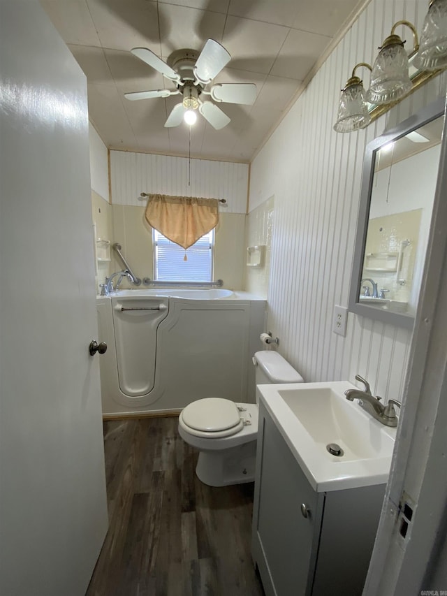 bathroom with toilet, hardwood / wood-style flooring, wooden walls, ceiling fan, and vanity