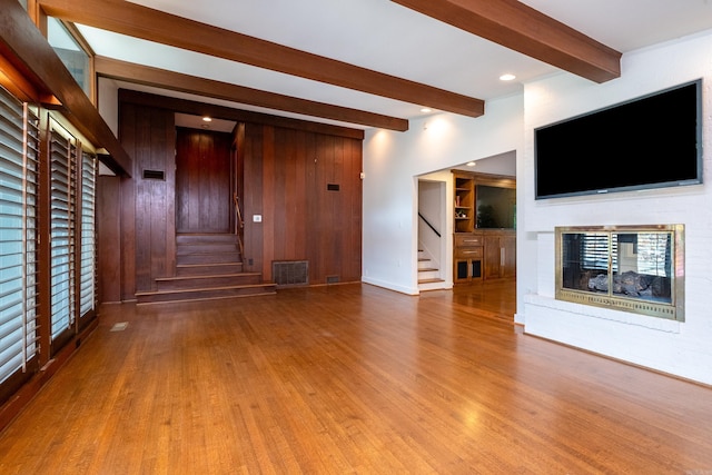 unfurnished living room with wood-type flooring, wooden walls, beamed ceiling, and a multi sided fireplace