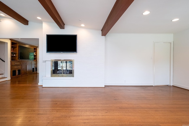 unfurnished living room featuring built in shelves, light hardwood / wood-style flooring, vaulted ceiling with beams, and a fireplace