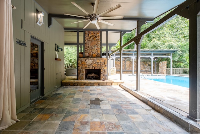 unfurnished sunroom featuring ceiling fan, an outdoor stone fireplace, and plenty of natural light