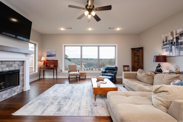 living room featuring ceiling fan, dark hardwood / wood-style flooring, and a stone fireplace