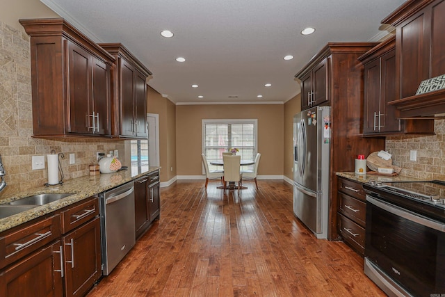 kitchen featuring stainless steel appliances, crown molding, light stone counters, decorative backsplash, and sink