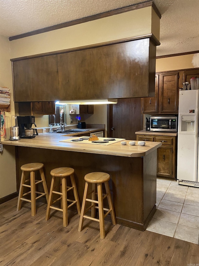 kitchen featuring a kitchen breakfast bar, a textured ceiling, kitchen peninsula, and white fridge with ice dispenser