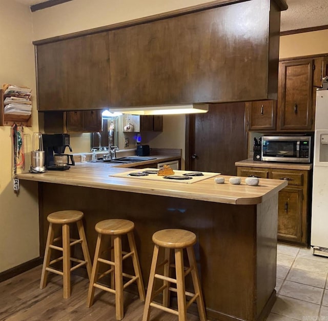 kitchen with sink, a kitchen bar, kitchen peninsula, dark brown cabinets, and white appliances