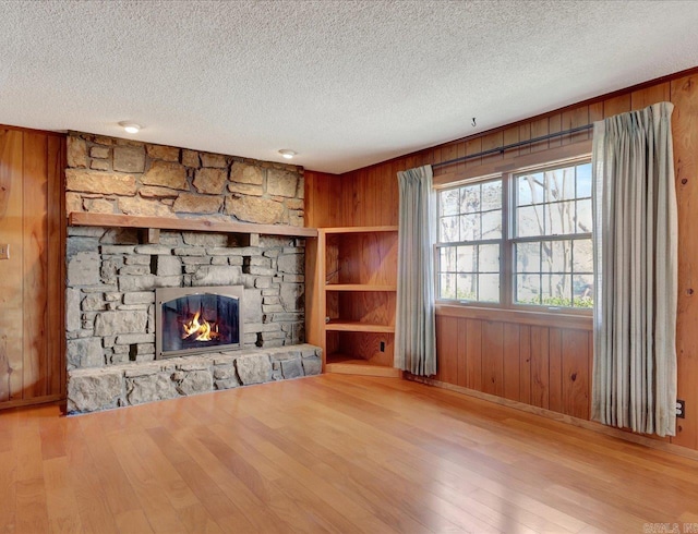 unfurnished living room with a textured ceiling, light wood-type flooring, wood walls, and a fireplace