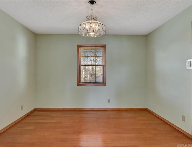 empty room with a textured ceiling, a notable chandelier, and light hardwood / wood-style floors