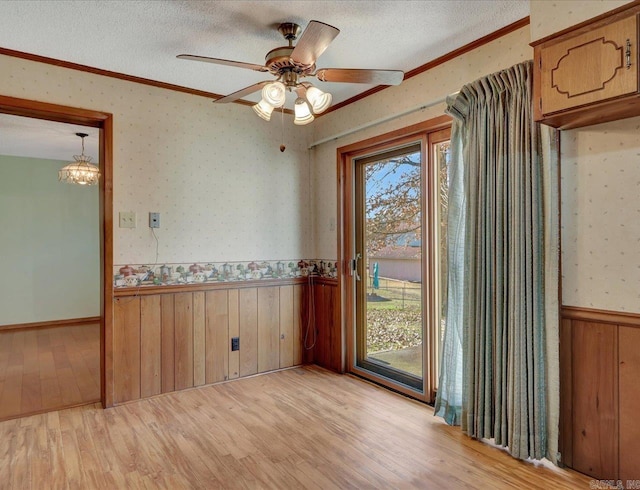 spare room featuring ceiling fan with notable chandelier, a textured ceiling, light wood-type flooring, and ornamental molding