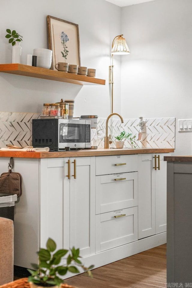 bar with sink, white cabinets, decorative backsplash, and light hardwood / wood-style floors