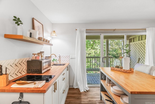 kitchen featuring dark wood-type flooring, wooden counters, black electric stovetop, white cabinetry, and sink