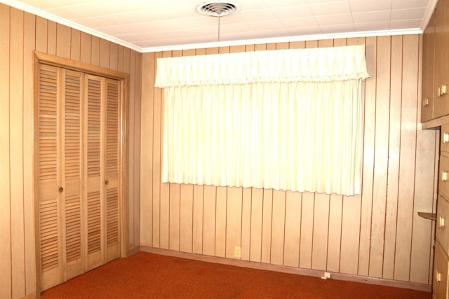 unfurnished bedroom with a closet, ornamental molding, carpet floors, and wooden walls