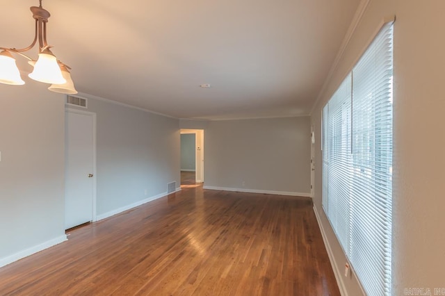 spare room featuring a chandelier, crown molding, and dark wood-type flooring