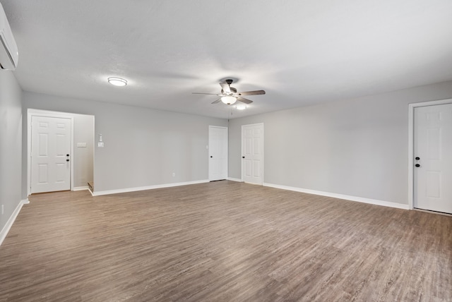 spare room with a wall mounted AC, ceiling fan, and wood-type flooring