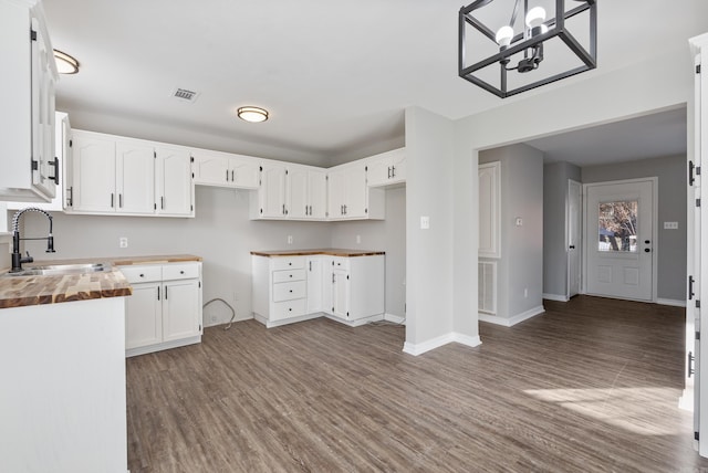 kitchen with wooden counters, an inviting chandelier, dark hardwood / wood-style flooring, white cabinetry, and sink