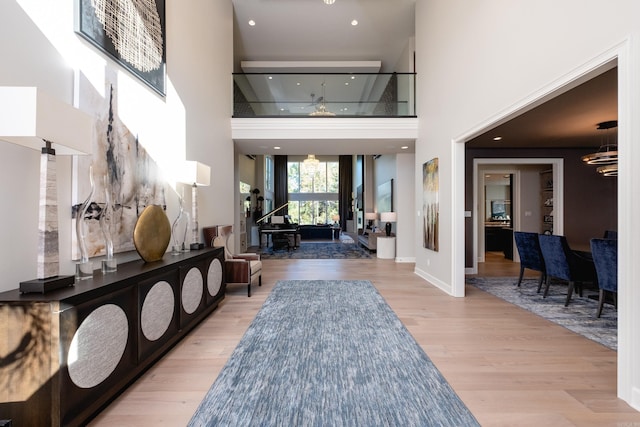 foyer with a towering ceiling, ceiling fan with notable chandelier, and light hardwood / wood-style flooring