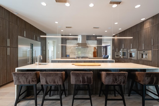 kitchen with a kitchen breakfast bar, a large island, wall chimney range hood, and pendant lighting